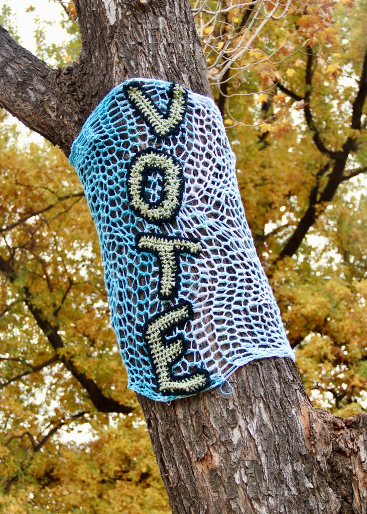 Vote written in yarn bombed crochet around a tree.